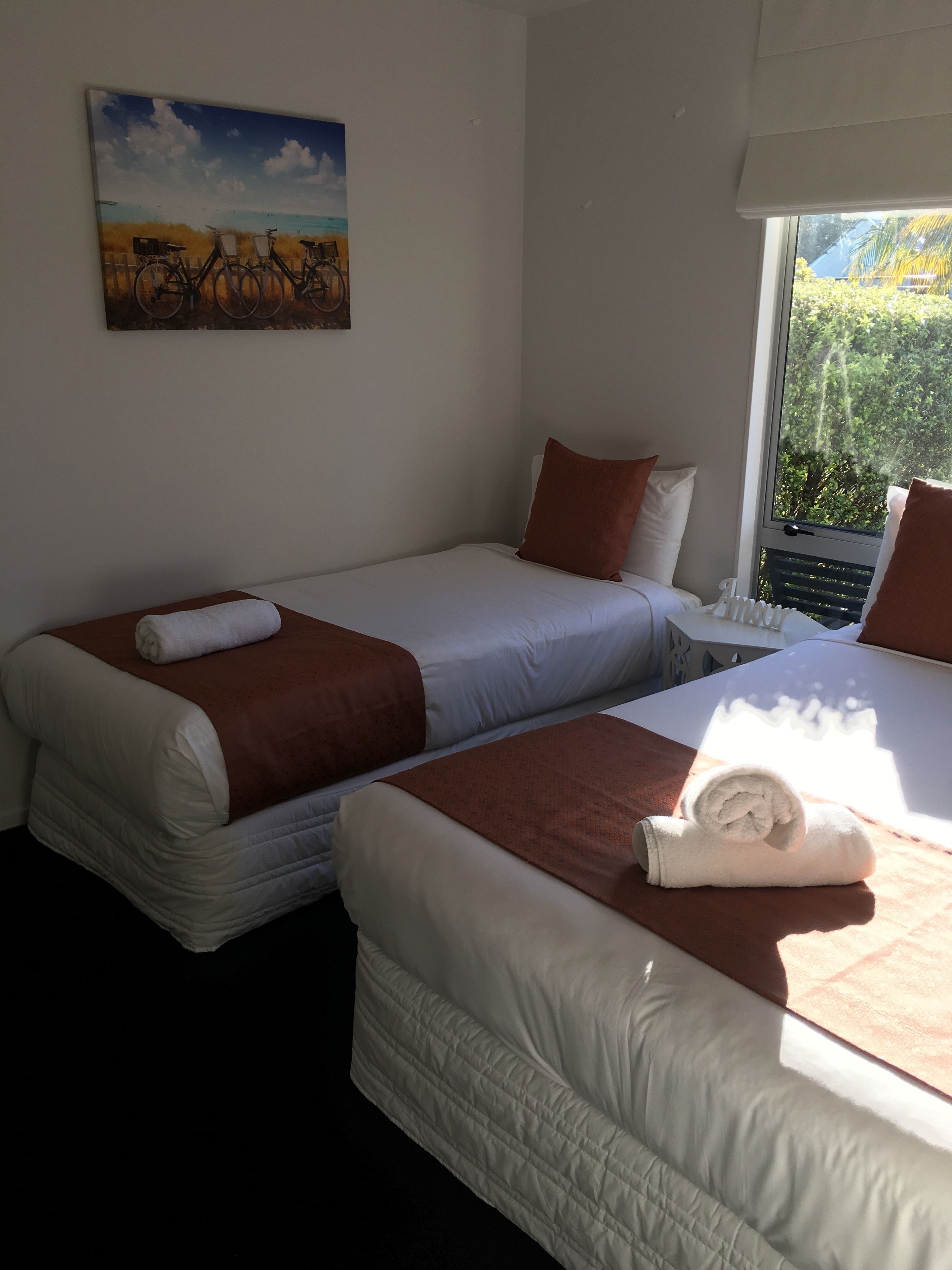 Une chambre d’hôtel avec deux lits simples, une fenêtre donnant sur un paysage verdoyant et un tableau accroché au mur.
