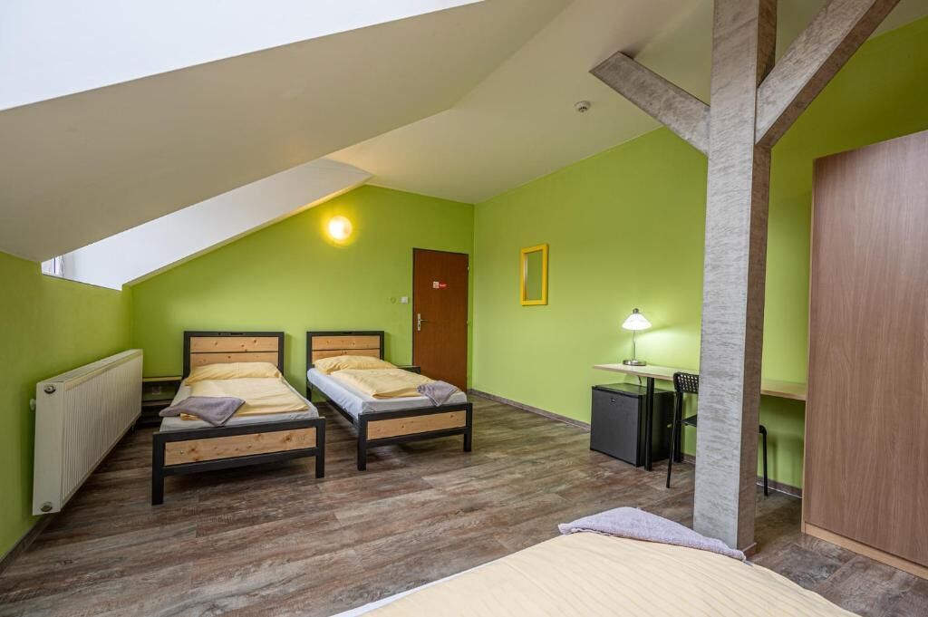 A room with two beds, a desk, a chair, a radiator, and a door.