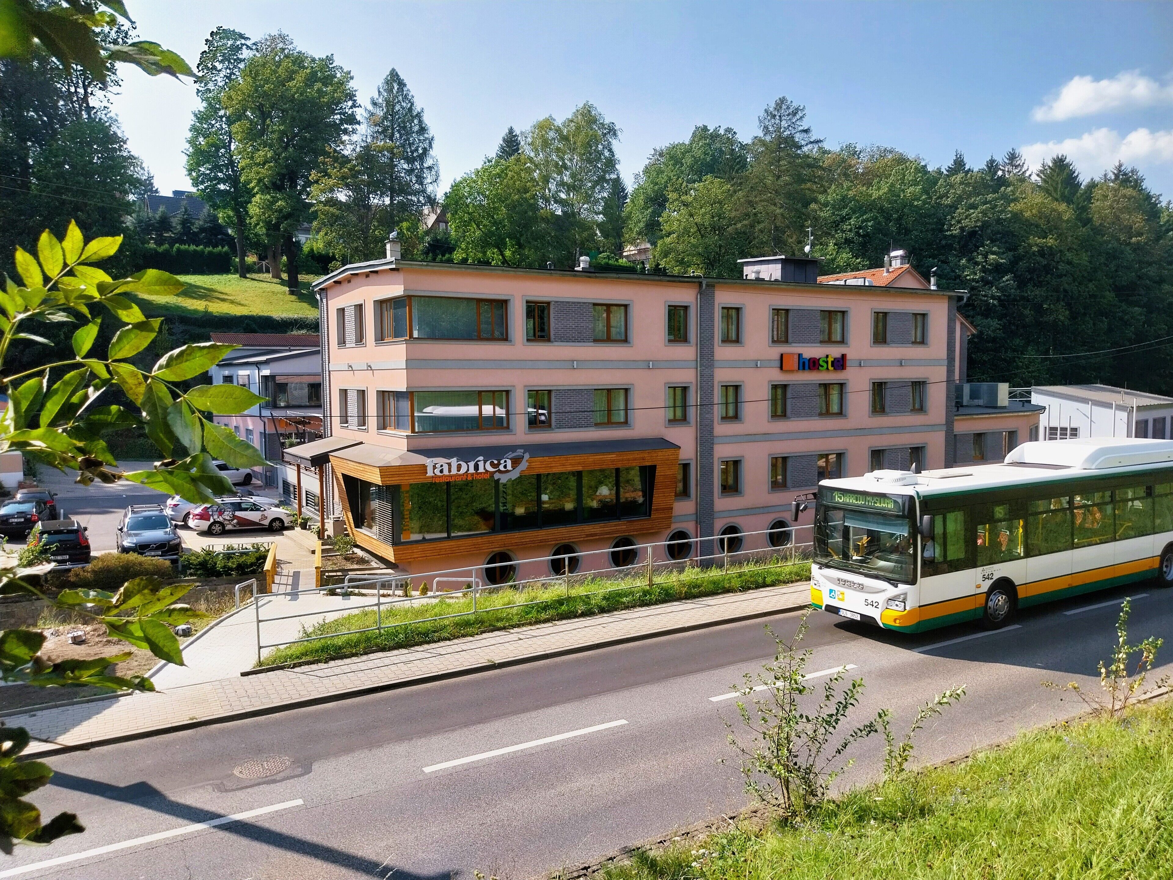 Un edificio de varios pisos con un letrero que dice 'hostel', un restaurante llamado 'Fabrica', y un autobús que pasa.