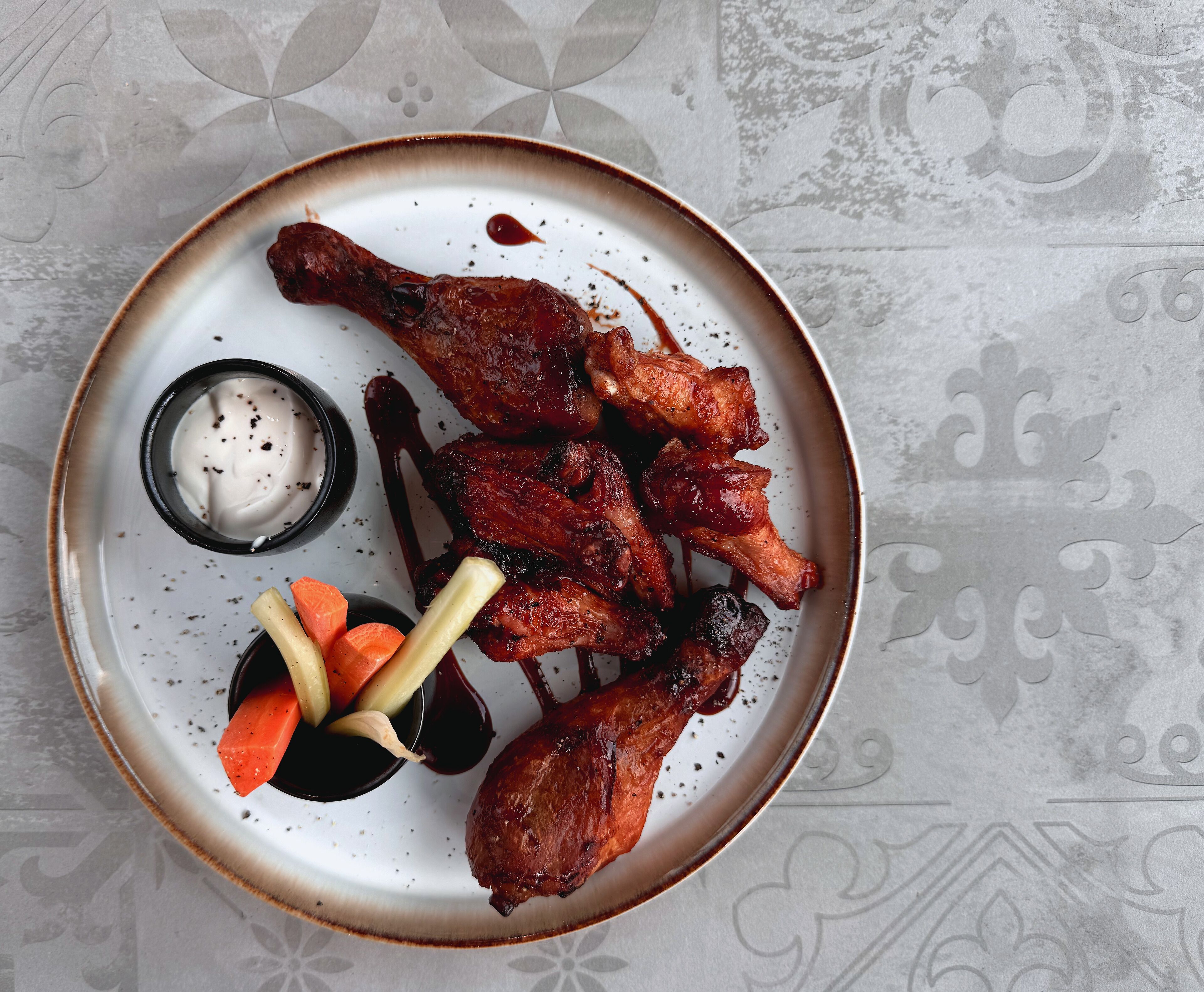 A plate with grilled chicken wings, a small bowl of sauce, and some vegetables.