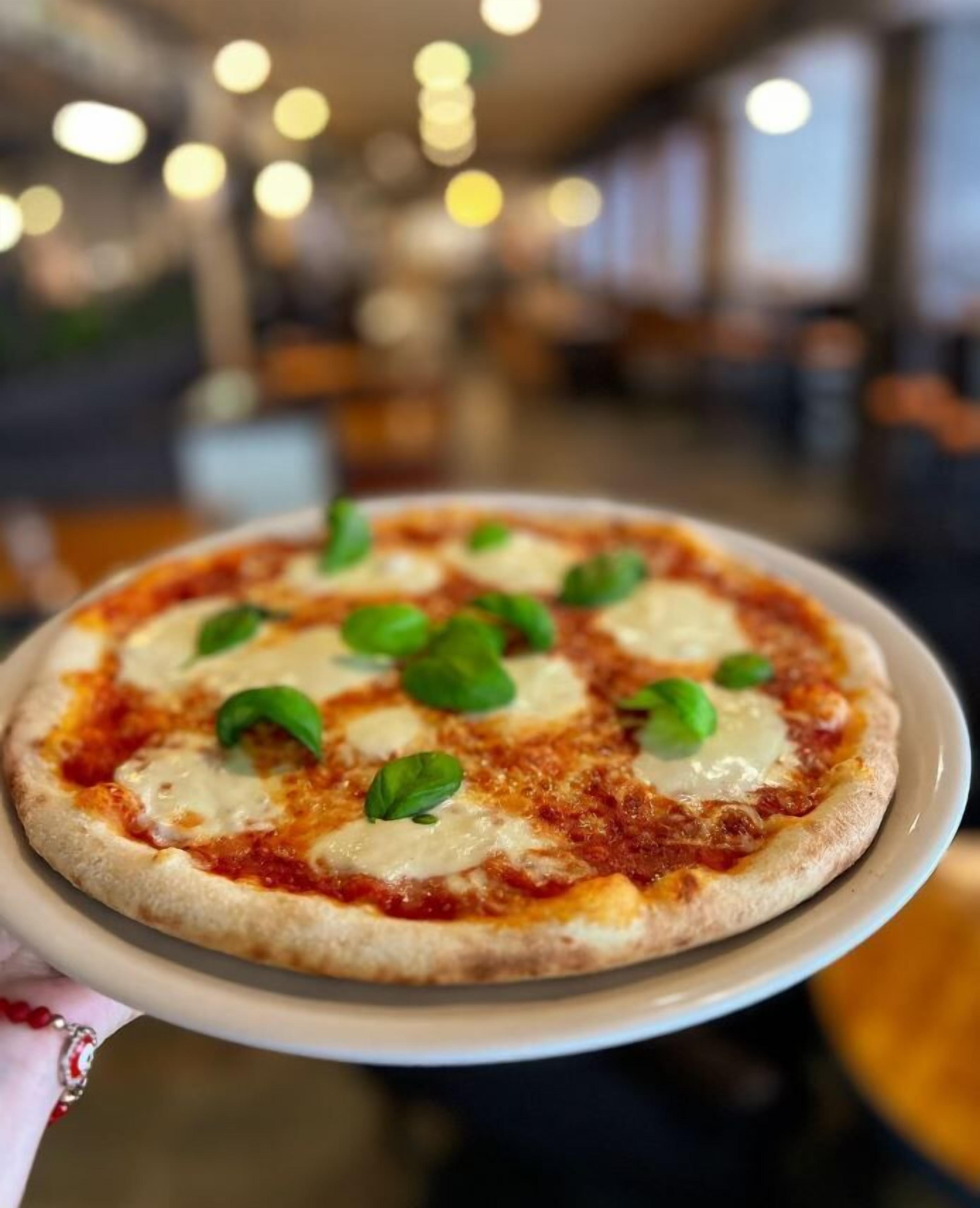 Una pizza con queso y albahaca sobre un plato blanco.