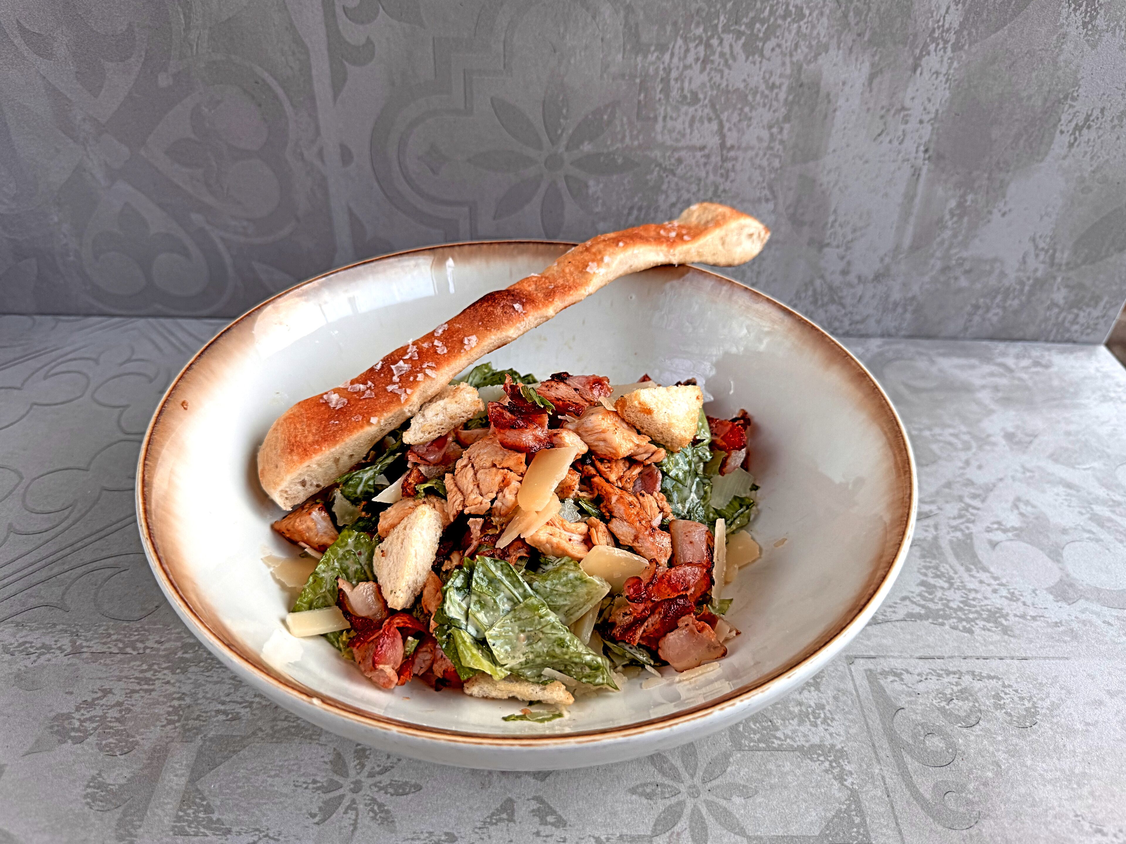 Ensalada con crutones y un trozo de pan sobre un mantel estampado.
