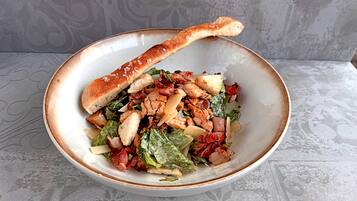 Ensalada con crutones y un trozo de pan sobre un mantel estampado.