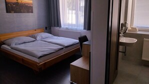 Une chambre d’hôtel comprenant un lit, un bureau, une chaise, une salle de bain avec un lavabo et une fenêtre avec des rideaux.