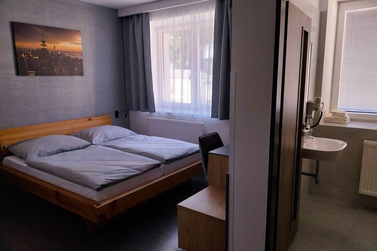 A hotel room with a bed, a desk, a chair, a bathroom with a sink, and a window with curtains.
