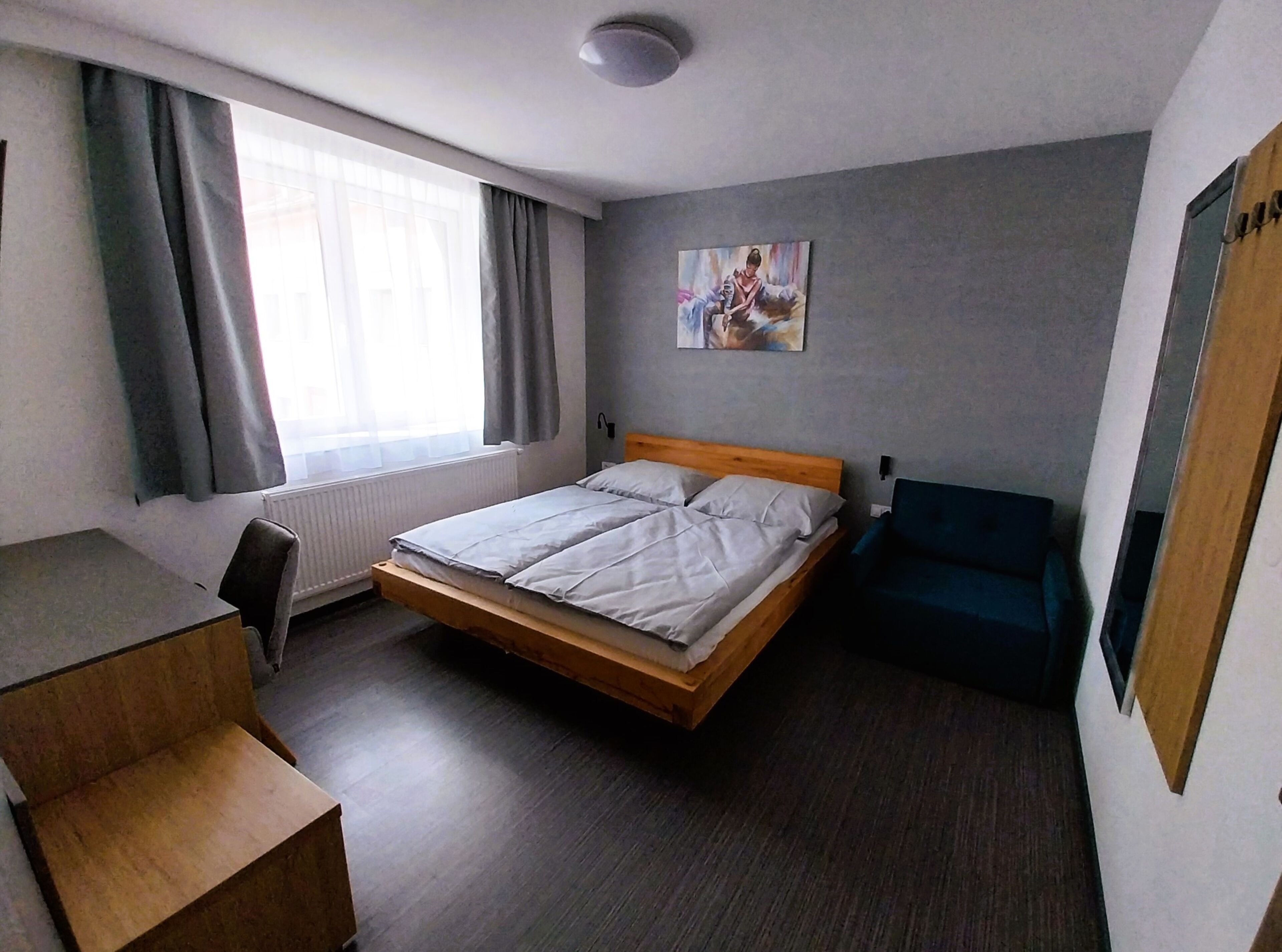 A hotel room with a single bed, a desk, a chair, and a window with curtains.