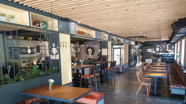 Un restaurant moderne avec un plafond et des murs en bois, doté de longues tables communes et de banquettes, et dont la cuisine est visible.