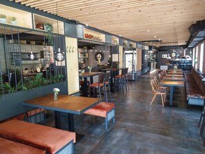 A modern restaurant with wooden ceiling and walls, featuring long communal tables and booths, and a visible kitchen area. - Hotel Fabrica (Liberec)