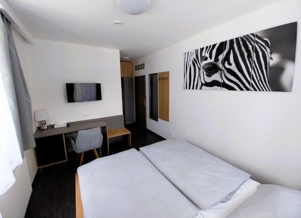 Habitación de hotel con cama, escritorio con televisor, un cuadro de cebra en la pared y ventana con cortinas.