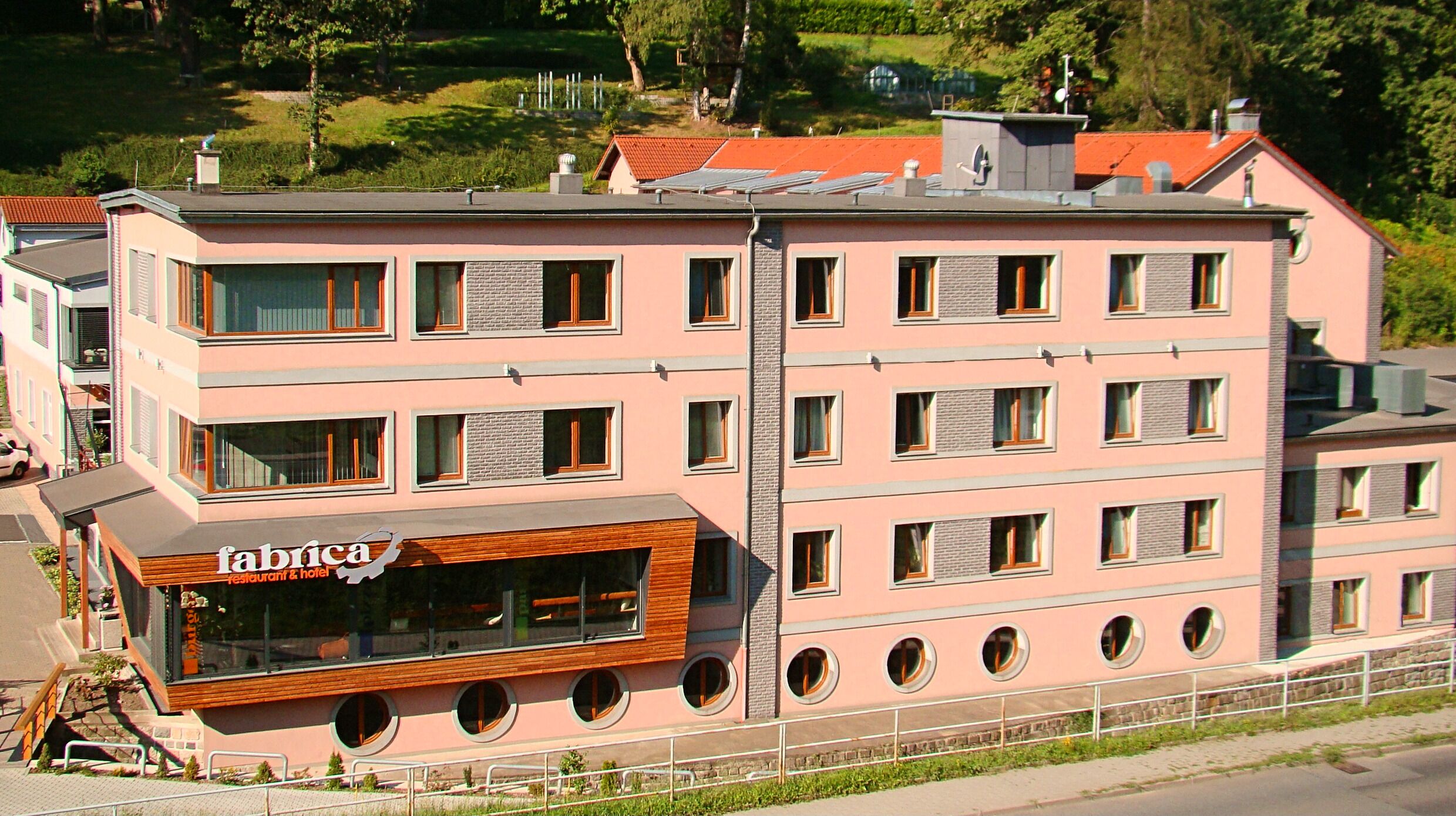 Un hotel de varios pisos con fachada rosa, múltiples ventanas y un restaurante en la planta baja.
