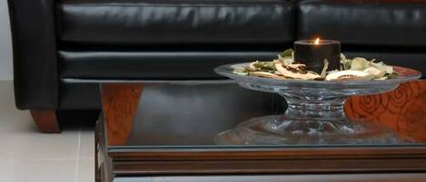 A black leather sofa with rose-patterned cushions, a glass coffee table with a candle, and a patterned rug.