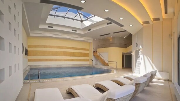 A modern indoor swimming pool with lounge chairs and a staircase leading to an upper level. - Delina Mountain Resort (Anogia)