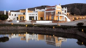 A modern building with multiple levels, a stone facade, and a reflection in a body of water. - Delina Mountain Resort (Anogia)