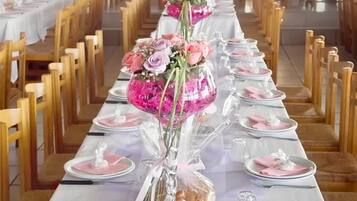 Una larga mesa de comedor con manteles rosas, cristalería transparente y centros de mesa con flores.