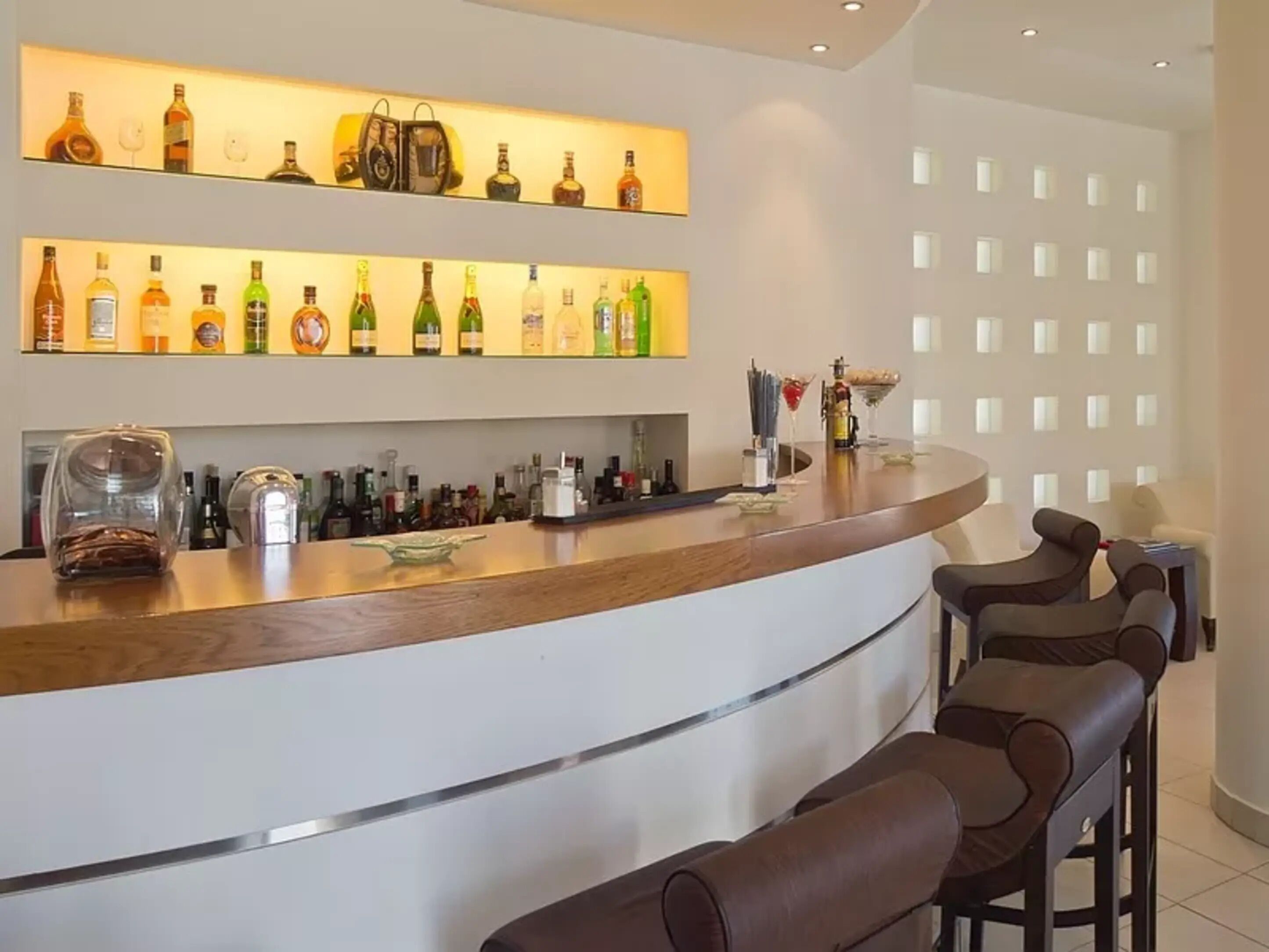 Un'area bar con un bancone curvo, diverse bottiglie di liquore e sgabelli da bar.