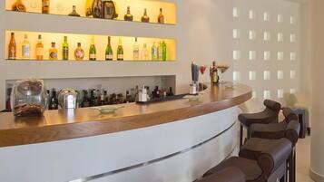 Un'area bar con un bancone curvo, diverse bottiglie di liquore e sgabelli da bar.
