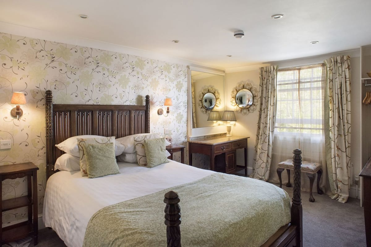 Une chambre à coucher avec un lit à baldaquin, une commode, une coiffeuse avec des miroirs et une fenêtre avec des rideaux.