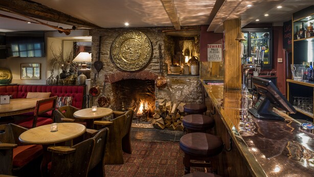 A cozy bar area with a stone fireplace, wooden furniture, and a variety of bottles and glasses on shelves. - Royal Seven Stars Hotel (Totnes)