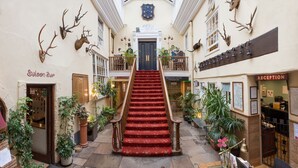 A hotel lobby with a central staircase, a reception desk, and a bar named 'Saloon Bar'. - Royal Seven Stars Hotel (Totnes)