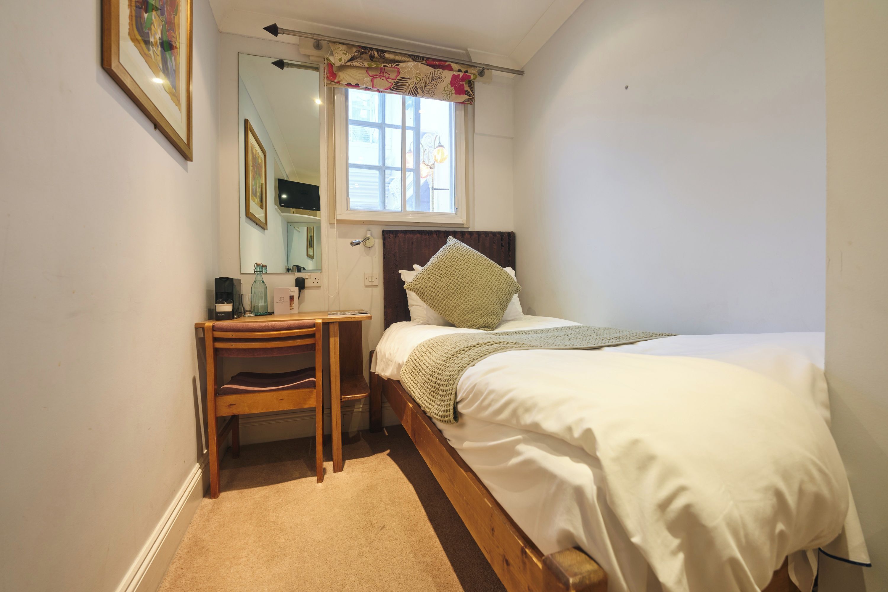 Quarto com uma cama, escrivaninha de madeira, espelho e janela com cortina.