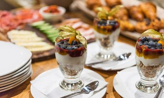 Una mesa de comedor con tres vasos para parfait, una pila de platos blancos y una cuchara de plata.