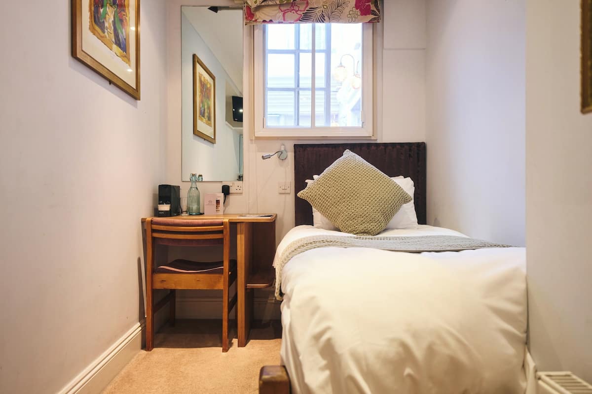 Une chambre à coucher avec un lit, une chaise en bois, une table de chevet, un miroir et une fenêtre.