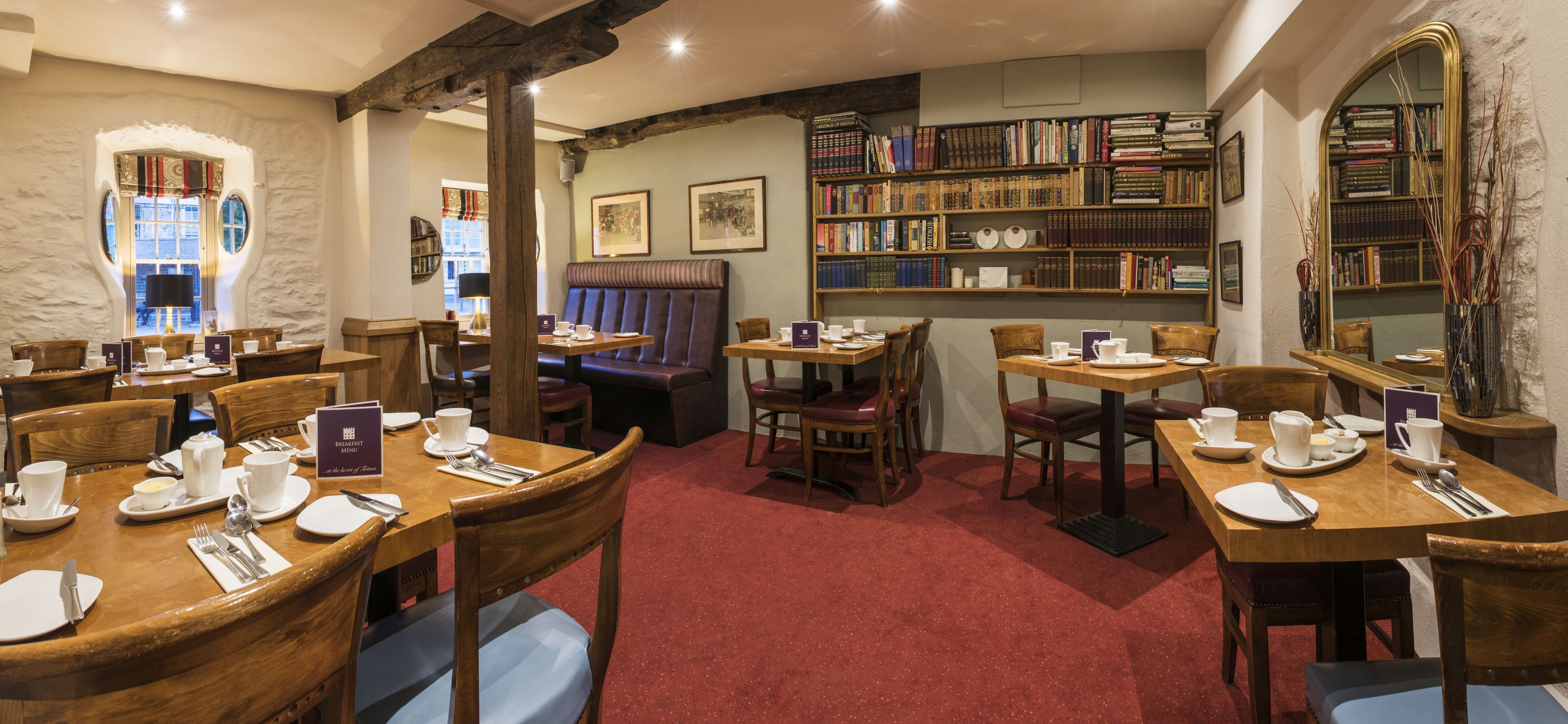 Un coin repas accueillant, avec des tables et des chaises en bois, une moquette rouge et une bibliothèque remplie de livres.