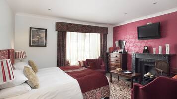 A hotel room with a large bed, a fireplace, a television mounted on the wall, and a desk with a lamp.