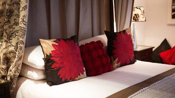 Un lit bien fait, avec du linge de lit blanc et des coussins décoratifs, dont de grandes fleurs rouges et un coussin noir et beige.