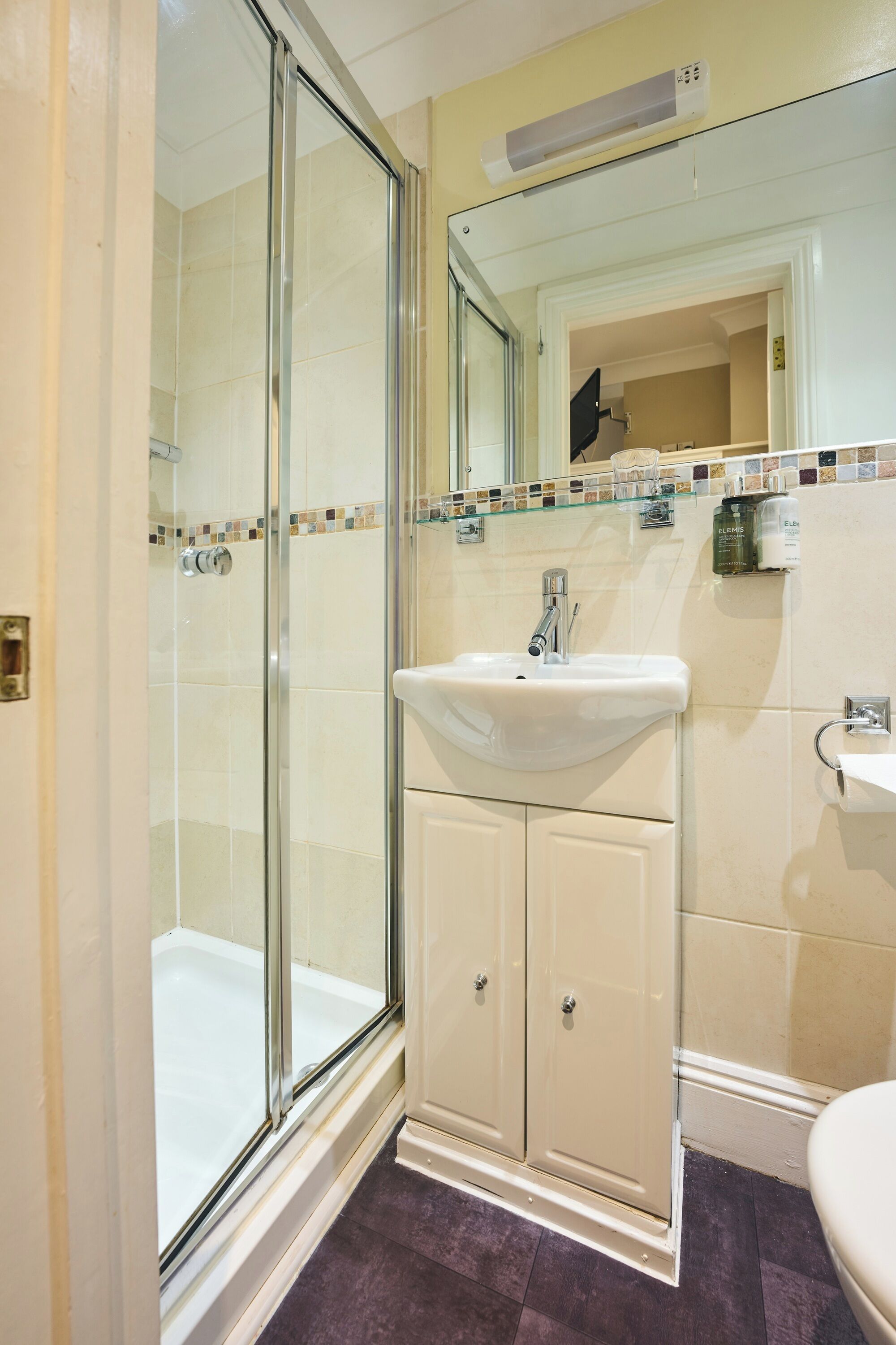 Un baño con cabina de ducha de vidrio, un lavamanos con espejo y un inodoro.