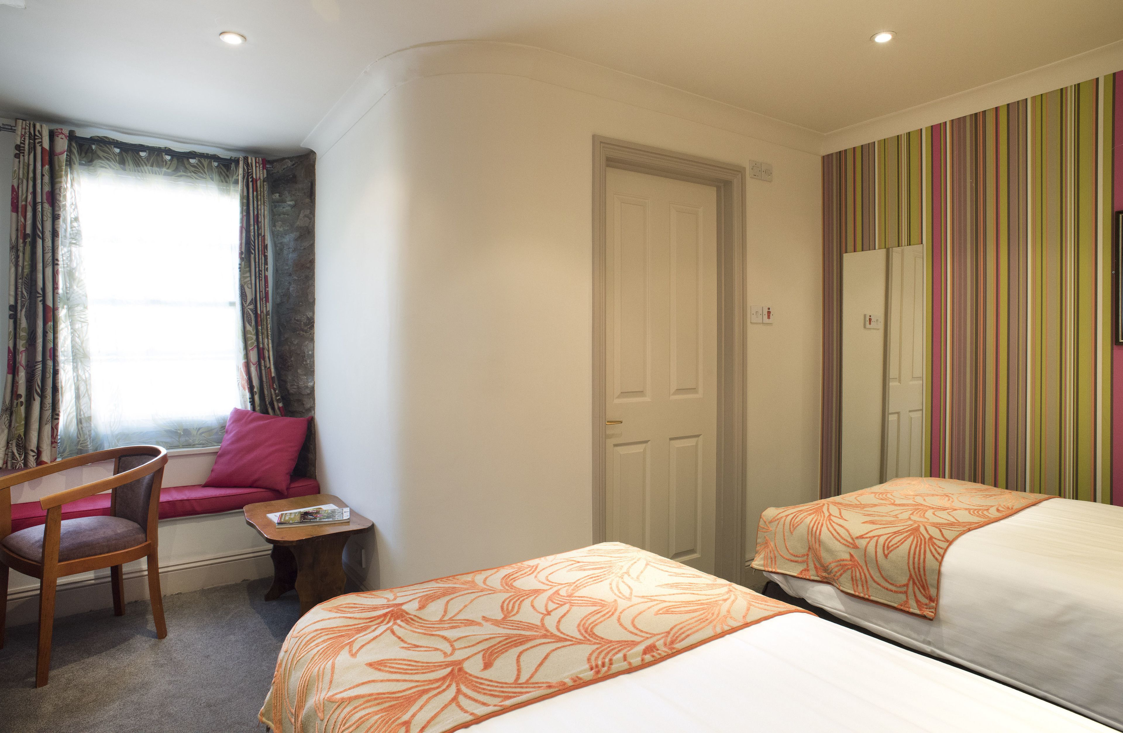 A hotel room with a window, a sofa, a chair, a small table, and two beds.