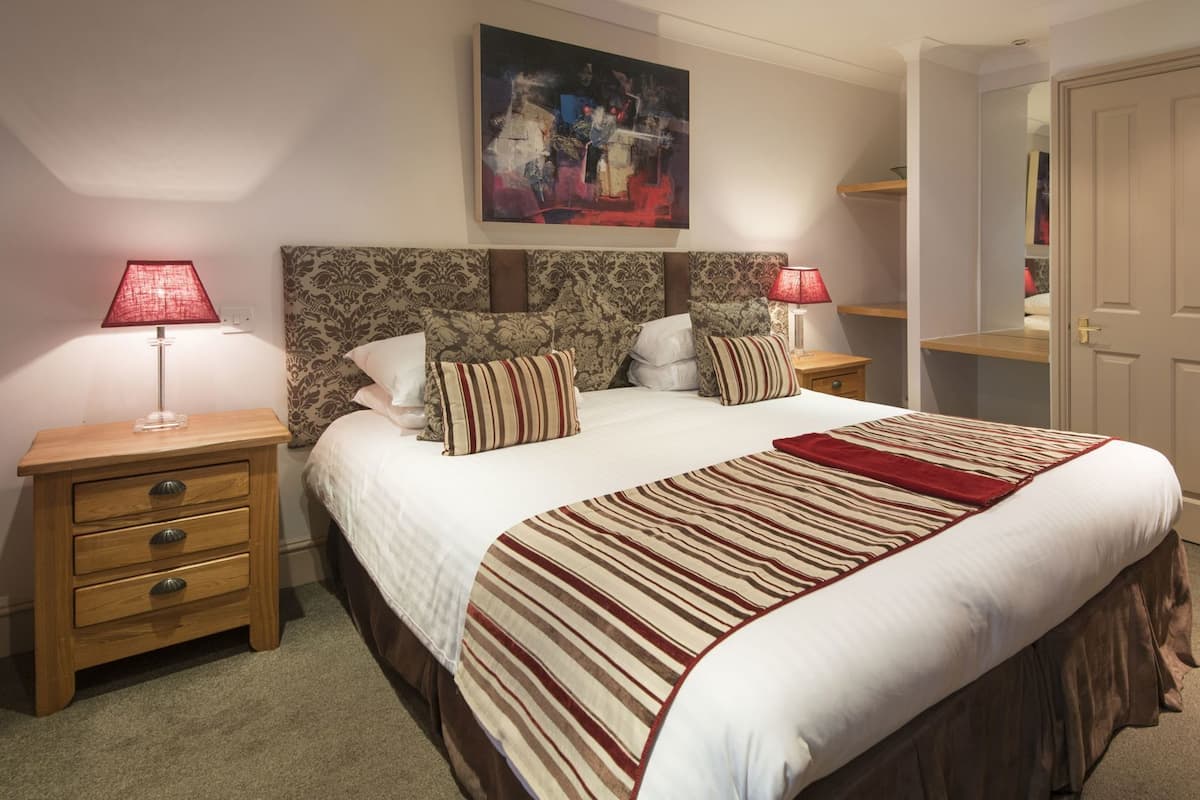 Une chambre à coucher avec un grand lit, deux tables de chevet, une commode, un tableau au mur et une porte.