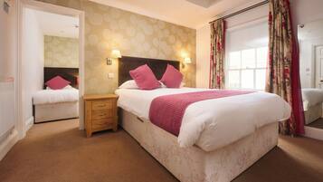A hotel room with a large bed, a wooden nightstand, a mirror, and a window with curtains.