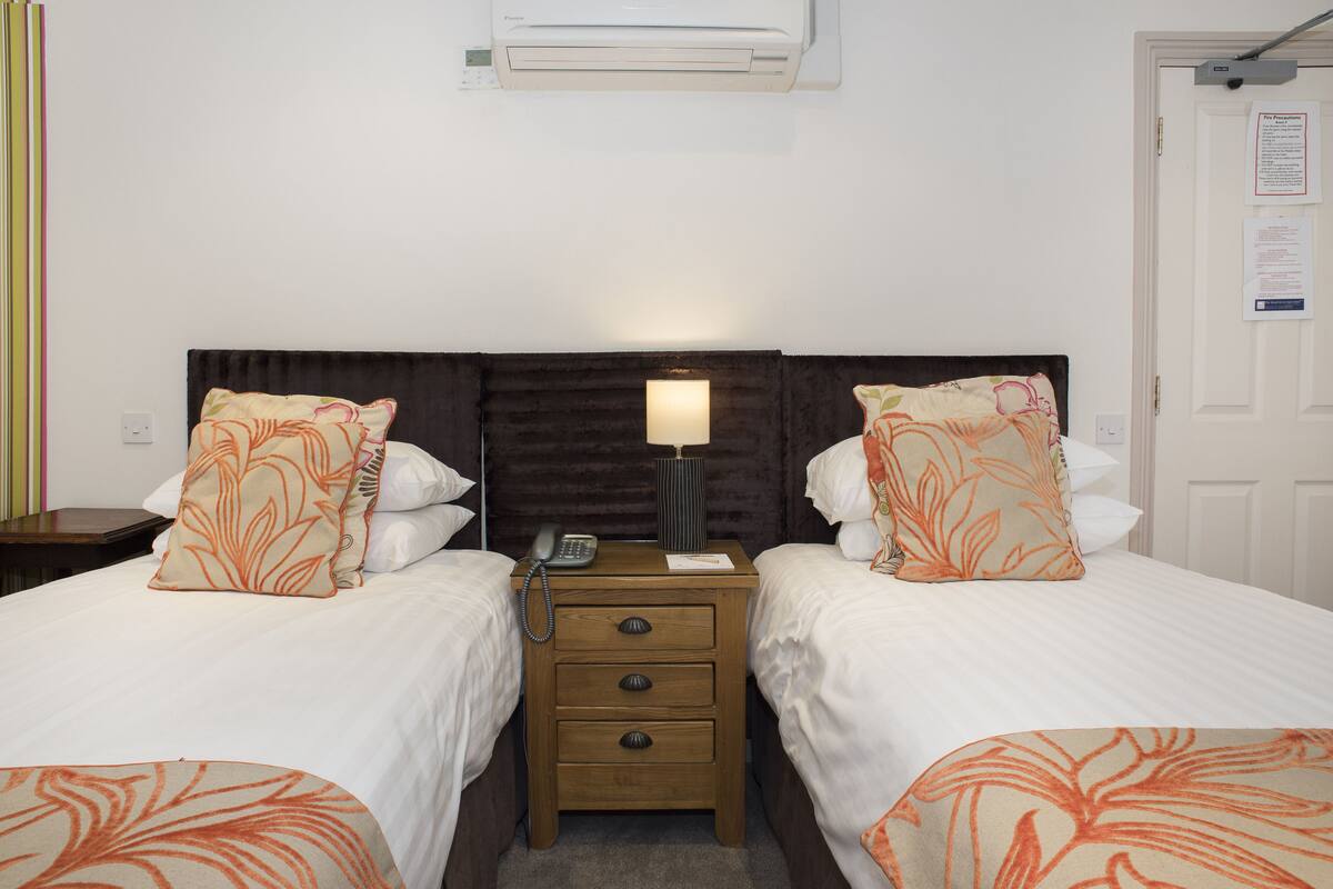 Une chambre d’hôtel avec deux lits, une table de chevet avec une lampe, un téléphone et un climatiseur fixé au mur.