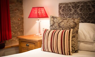 A neatly made bed with striped pillows, a red lamp on a bedside table, and a patterned headboard.