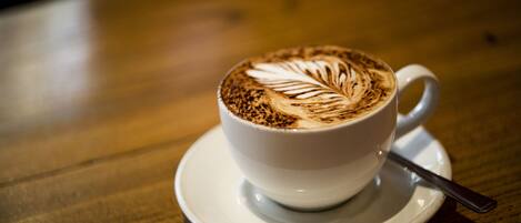 Una taza blanca de café con arte de latte sobre una mesa de madera.