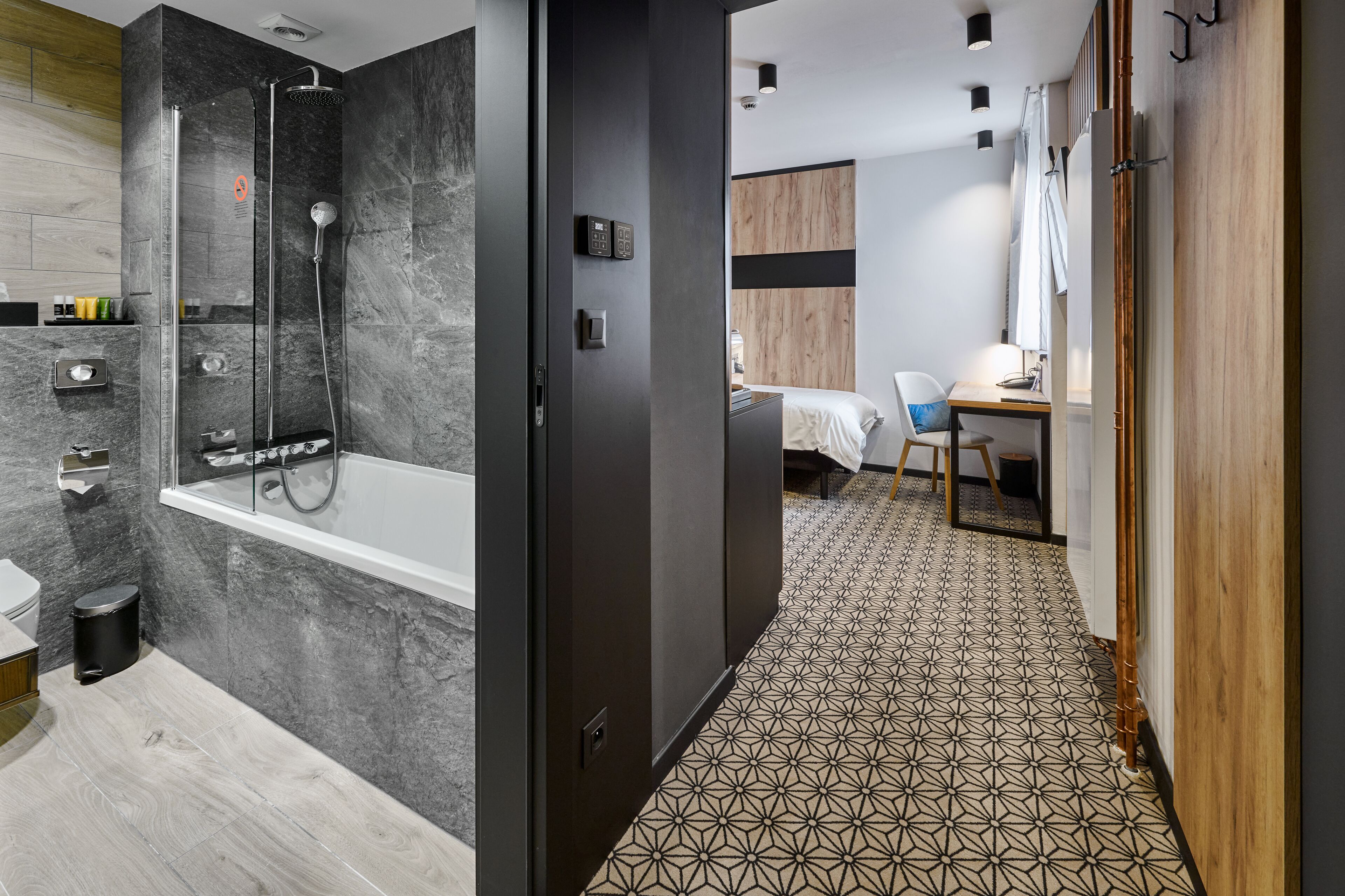 A modern bathroom with a shower, toilet, and sink; a bedroom with a bed and desk; and a hallway with patterned flooring.
