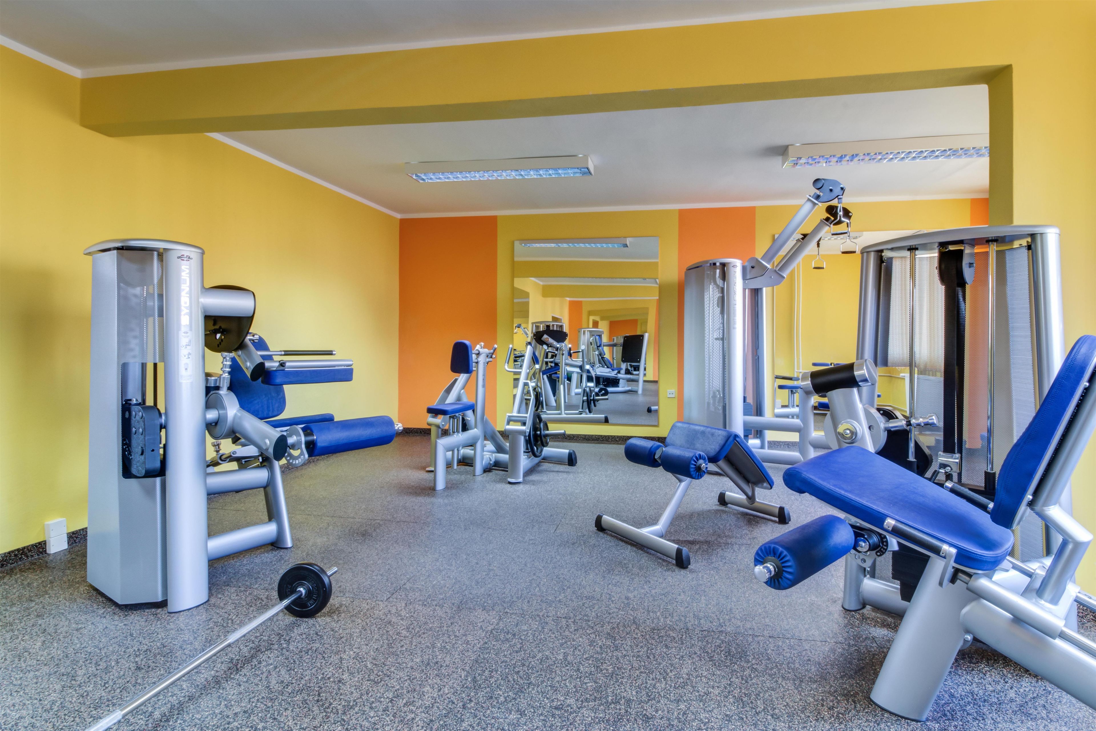 Een sportschool met diverse fitnessapparaten, waaronder krachttoestellen en losse gewichten, en een spiegel die de ruimte weerspiegelt.