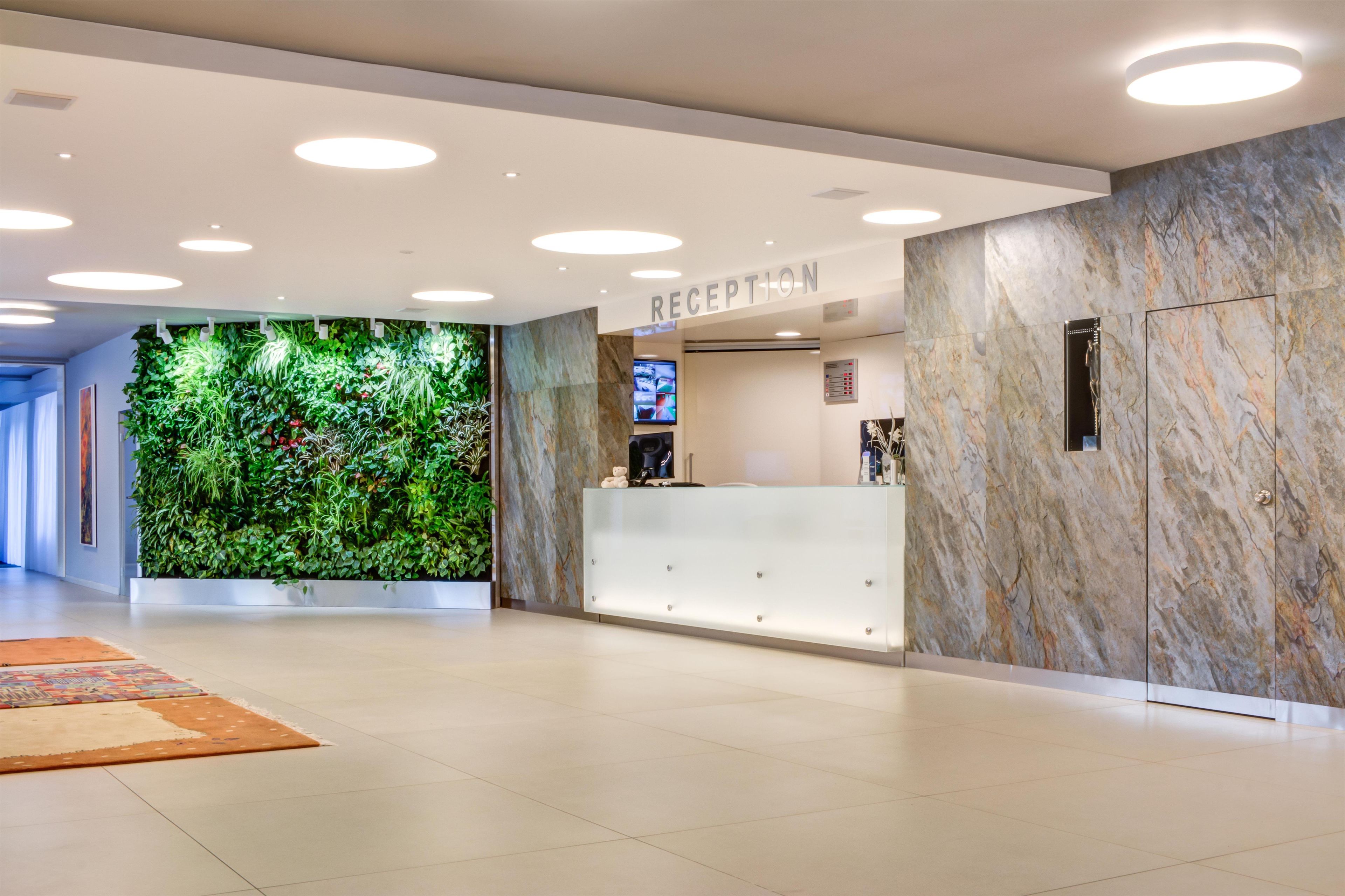 A reception area with a marble wall, a green plant wall, and a reception desk.