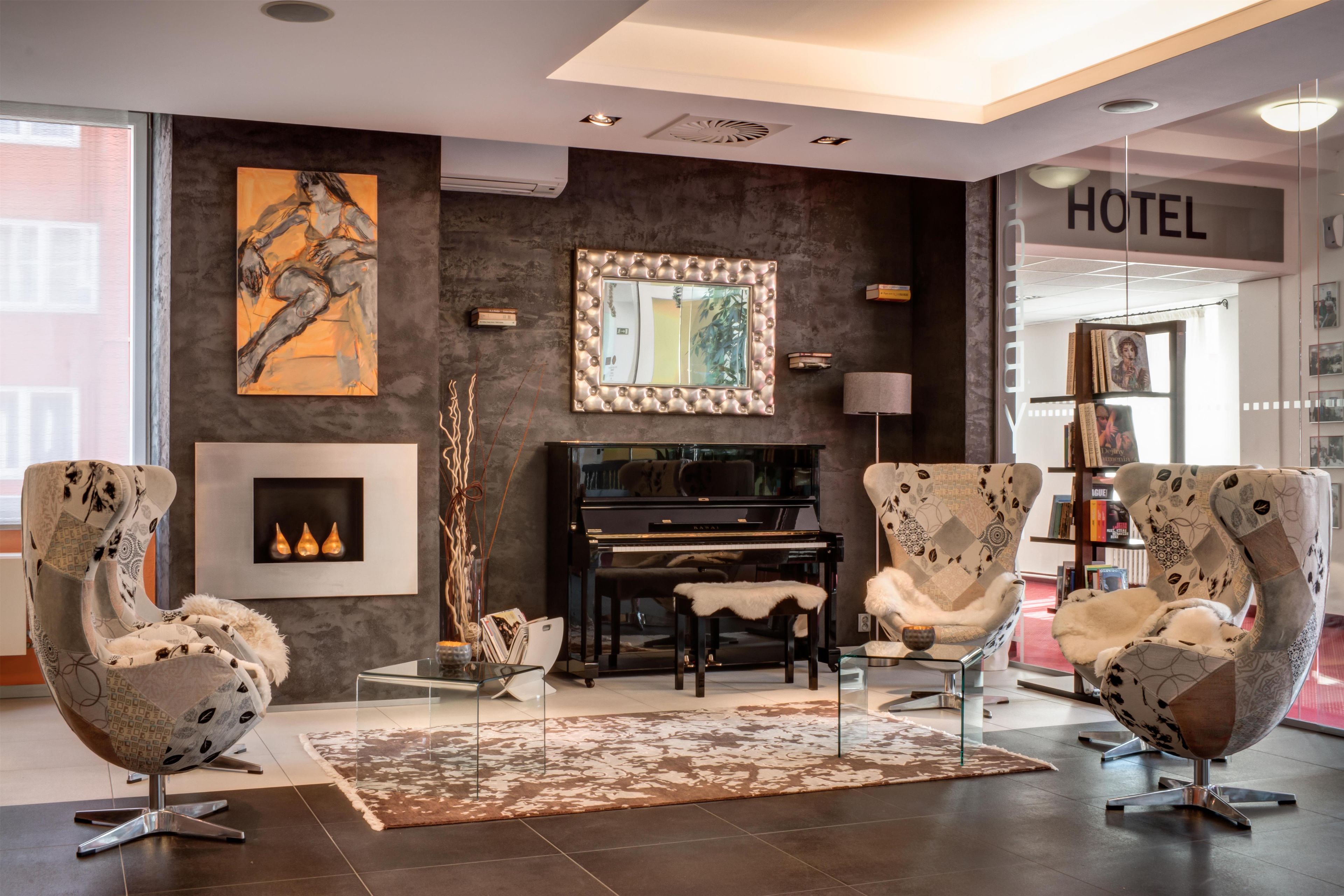 Een moderne hotel lobby met een vleugelpiano, comfortabele zithoek en een groot schilderij aan de muur.