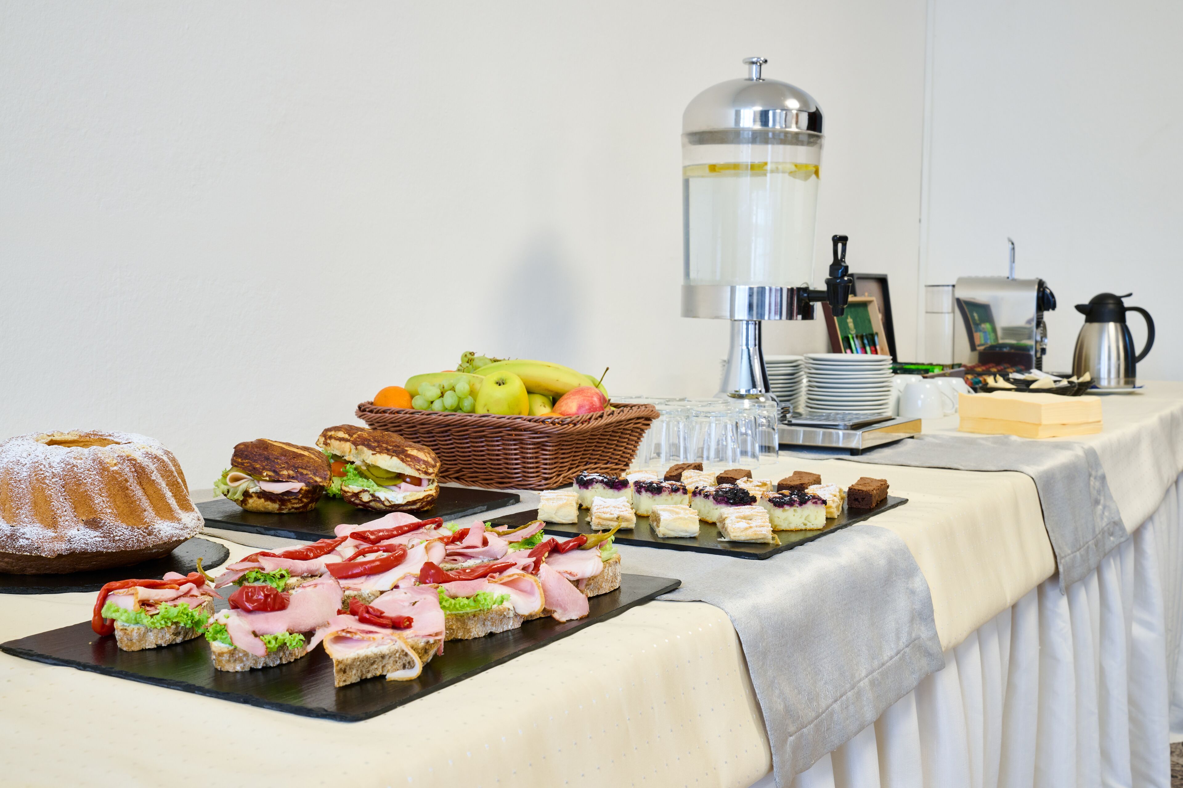 Una mesa de buffet con diversos alimentos, un dispensador de agua y una máquina de café.