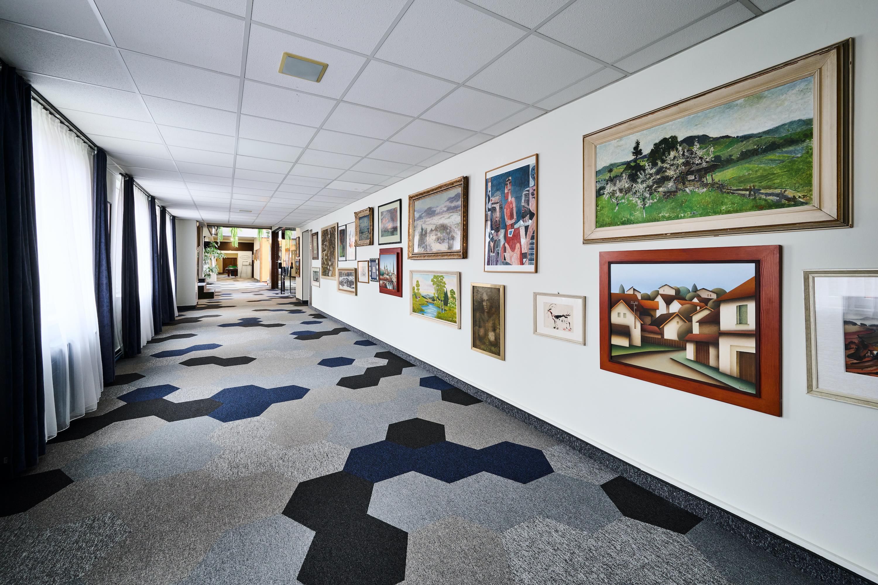 A hallway with artwork on the walls, a patterned carpet, and a view of the lobby area.
