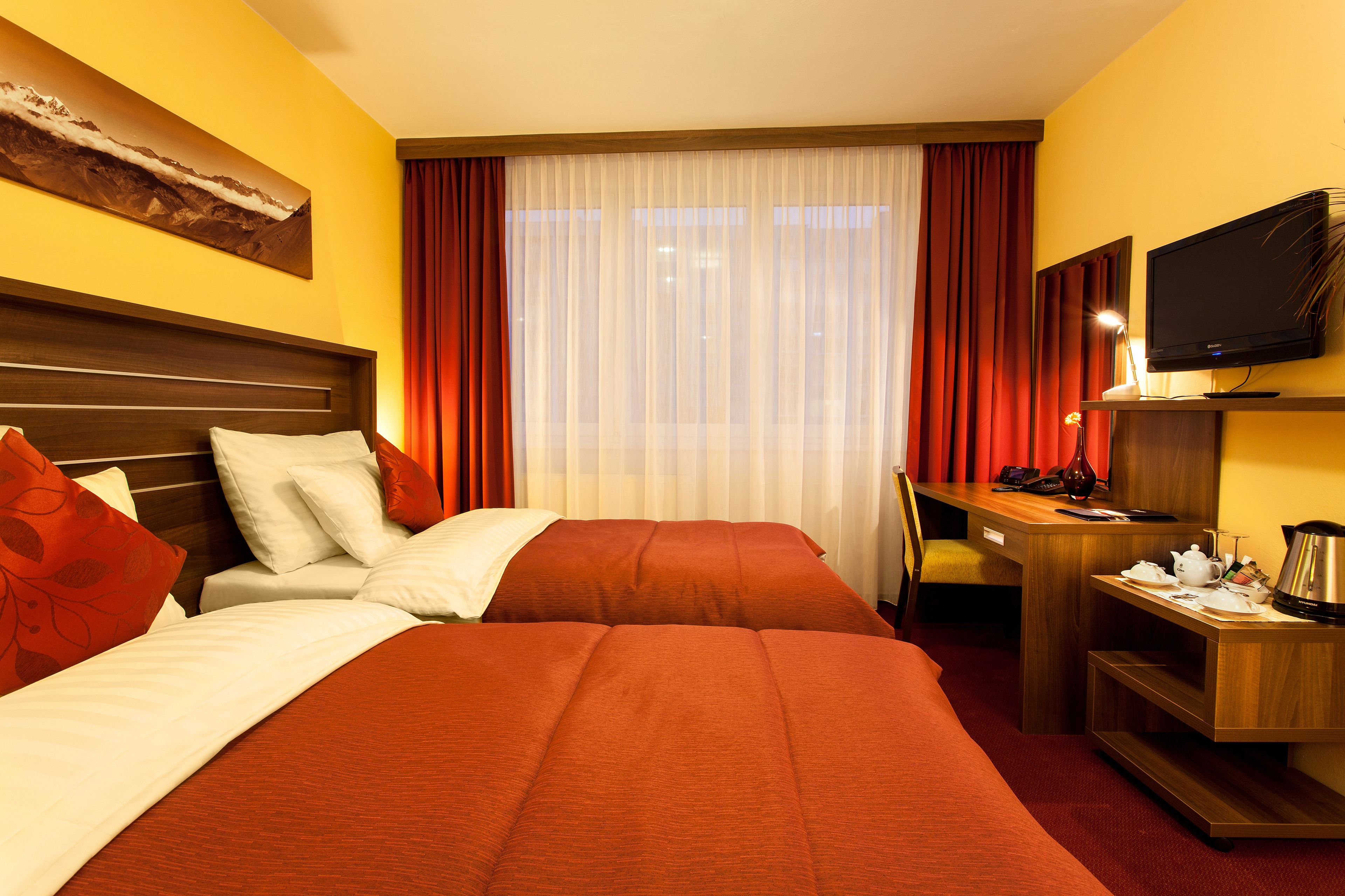 A hotel room with two beds, a desk, a television, and a window with curtains.