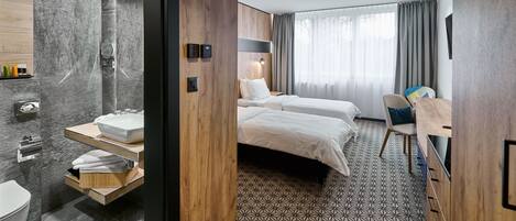 A modern hotel room with a large bed, a desk, a chair, a bathroom with a sink and toilet, and a large window with curtains.