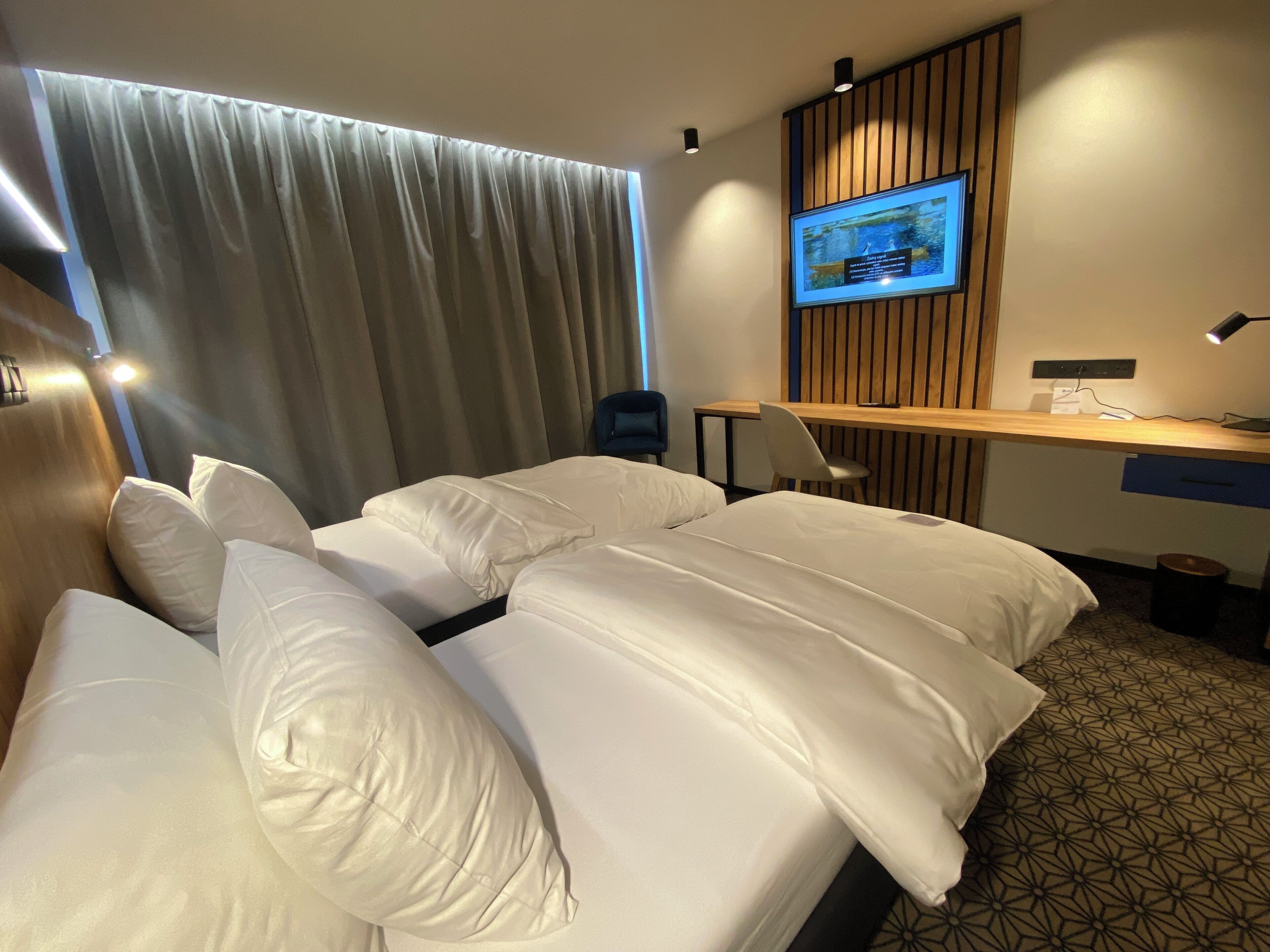 A hotel room with two beds, a desk, a chair, a TV mounted on the wall, and a curtain.