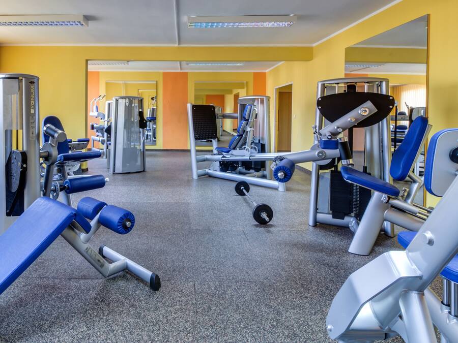 A gym with various exercise machines, a mirrored wall, and a carpeted floor.