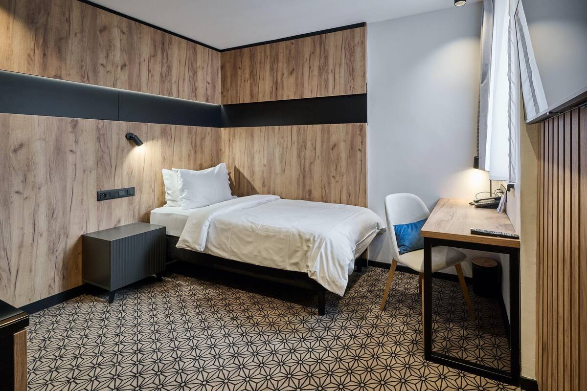 A modern bedroom with a bed, bedside table, and a desk with a chair.