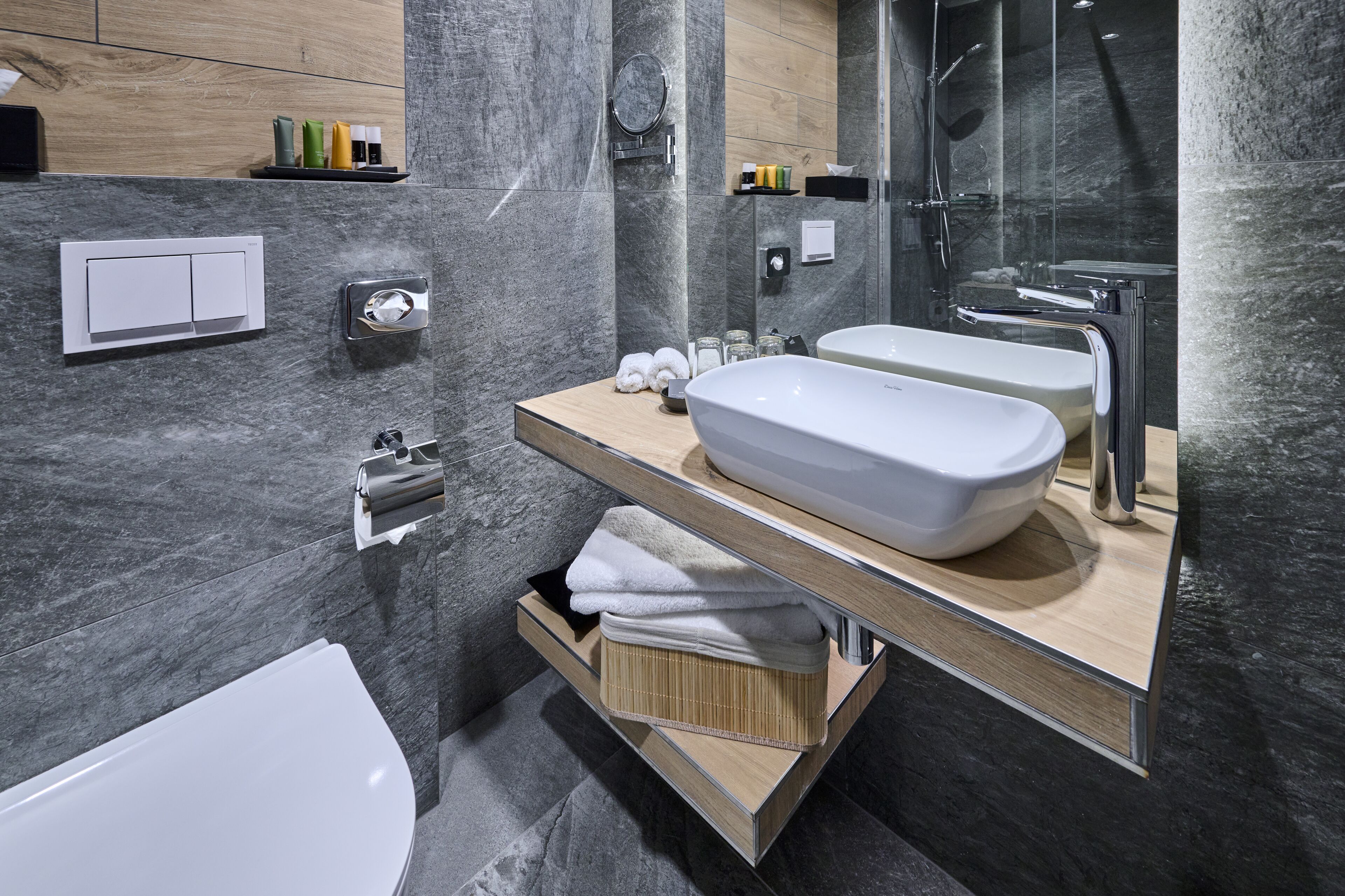 A modern bathroom with a large mirror, two sinks, a shower, and a towel rack.