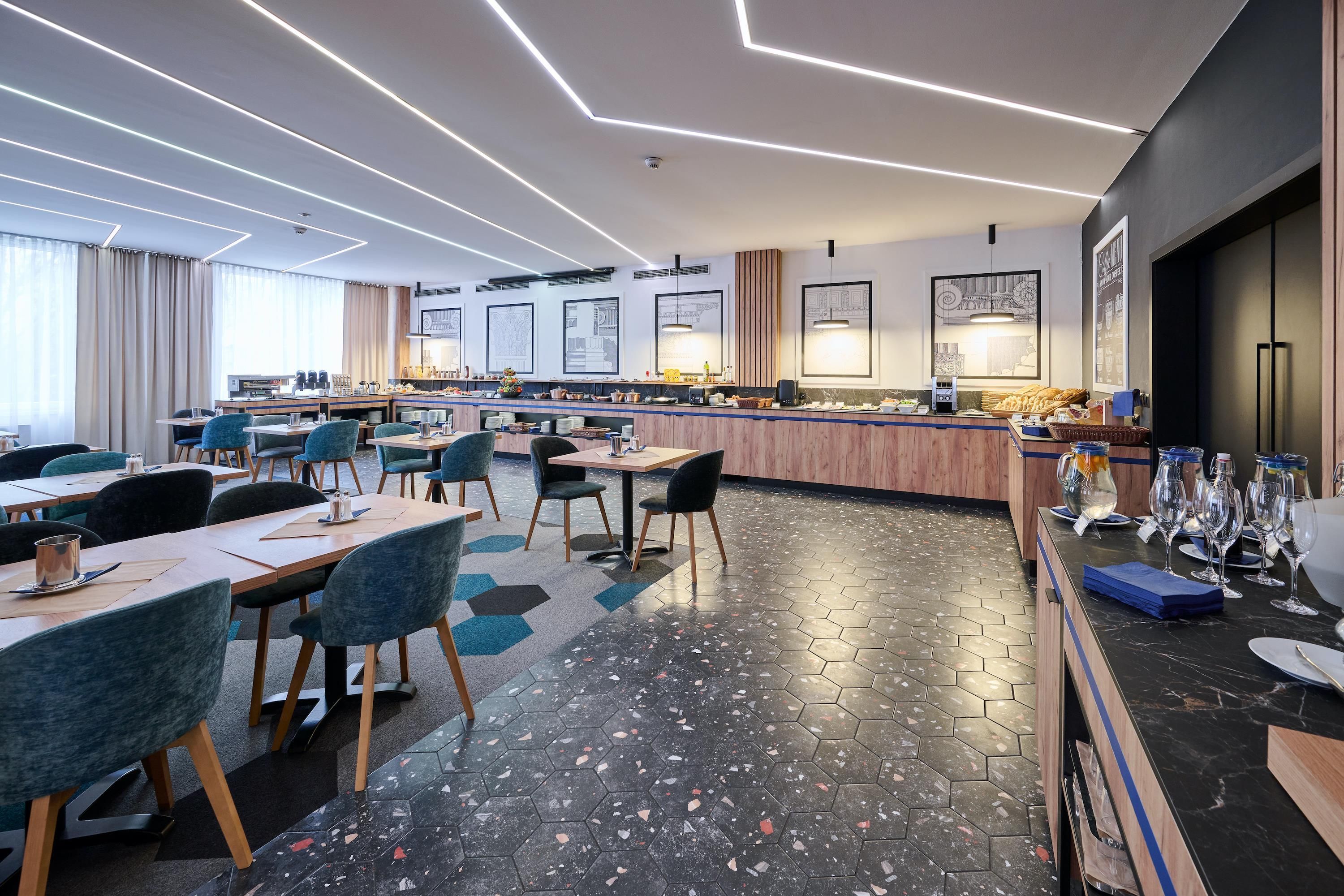 Un hall d’hôtel moderne avec un sol à motifs hexagonaux, un bar central et des espaces aménagés pour s’asseoir.