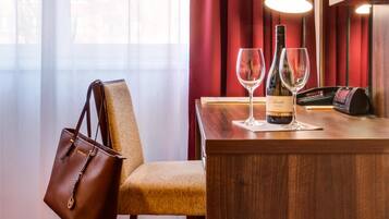 A hotel room with a wooden desk, a chair, a handbag, a bottle of wine, and a wine glass.